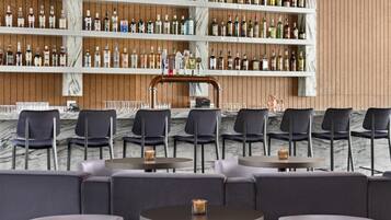A bar area with multiple shelves of liquor bottles, round tables with chairs, and a marble wall.