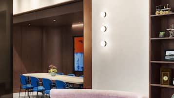 A modern conference room with a long table, blue chairs, and a bookshelf with awards.