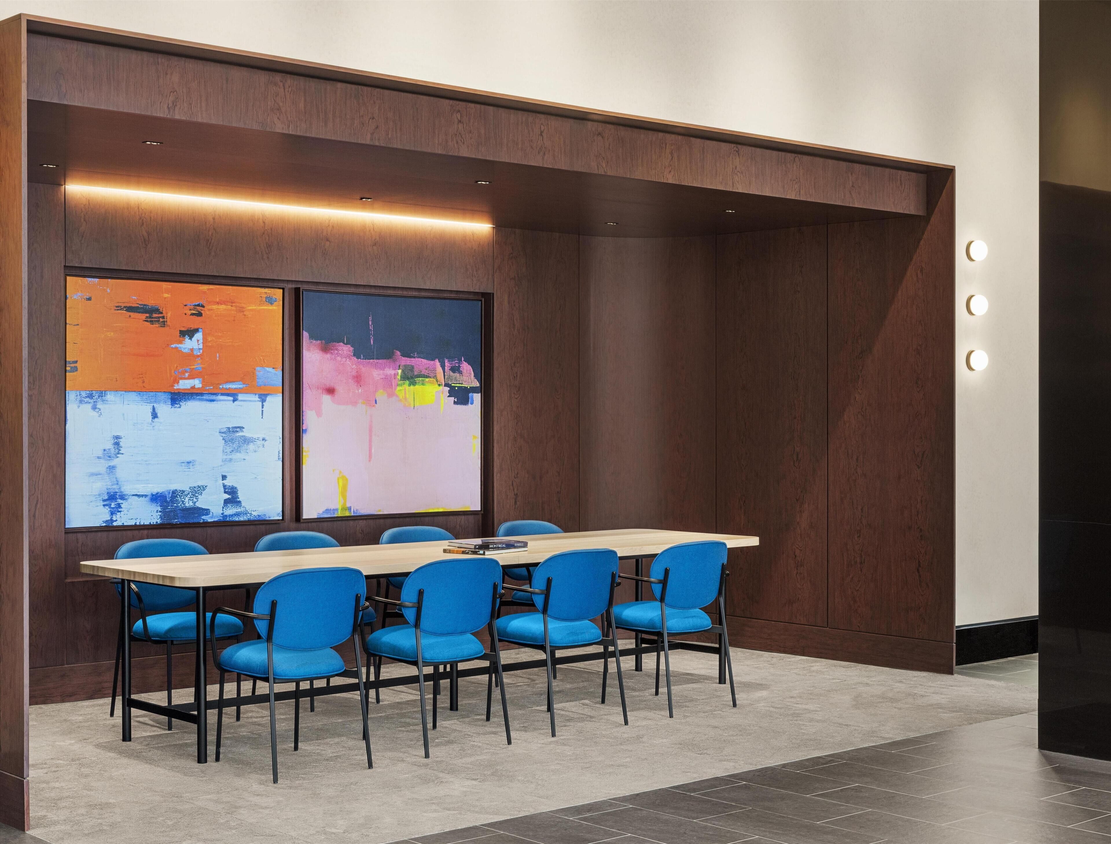 A conference room with a long table, blue chairs, and a large abstract painting on the wall.