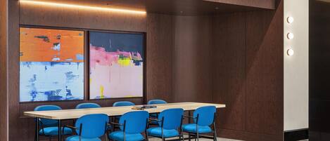 A conference room with a long table, blue chairs, and a large abstract painting on the wall.
