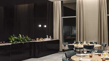 Un comedor moderno con una barra negra, plantas verdes y una mesa preparada para cuatro personas, con vasos y cubiertos.