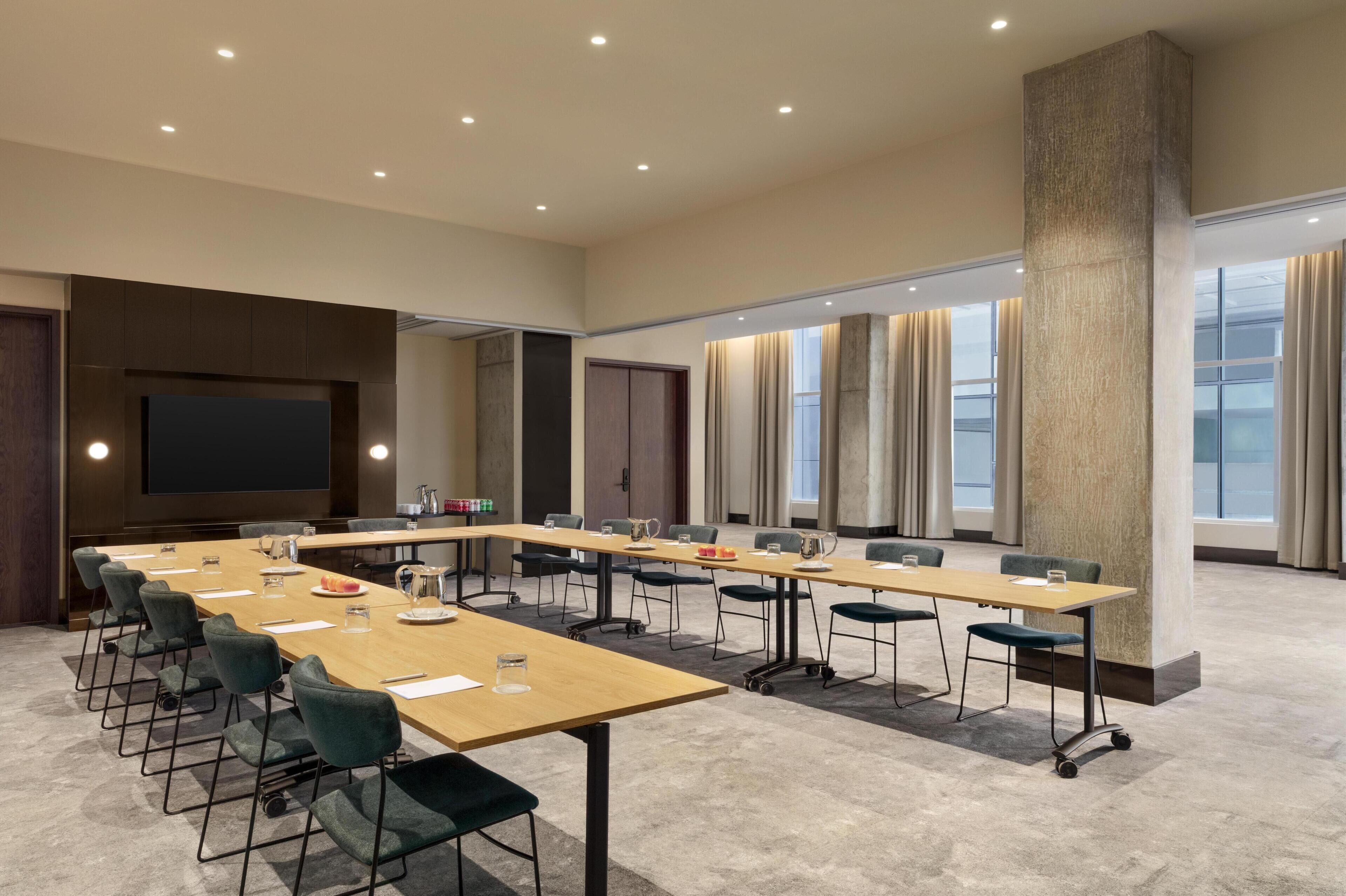 A conference room with a long table, chairs, a screen, and windows.