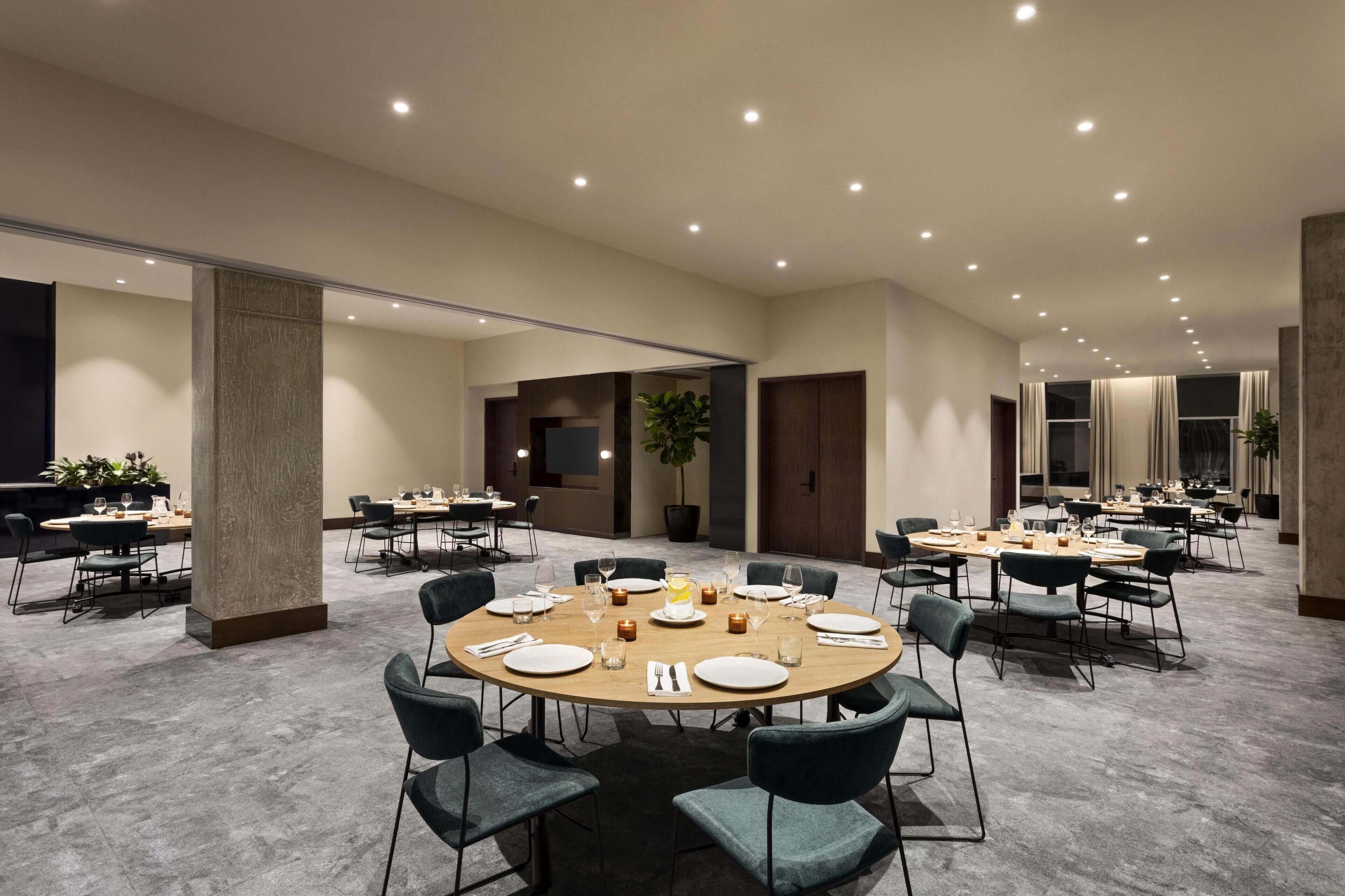 Un salón de conferencias con mesas redondas, sillas y una planta grande.