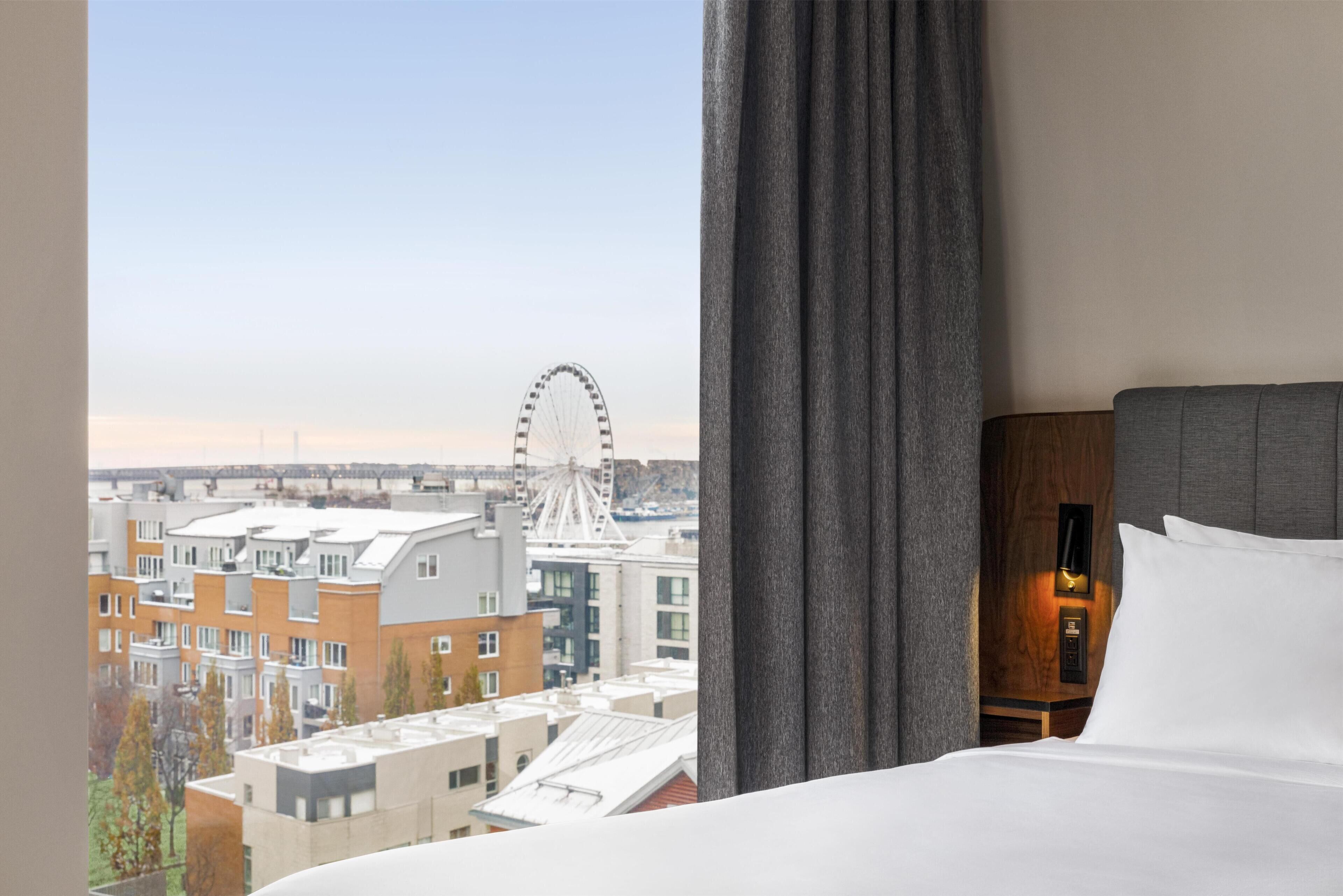 Een hotelkamer met een bed, nachtkastje en uitzicht op een reuzenrad.