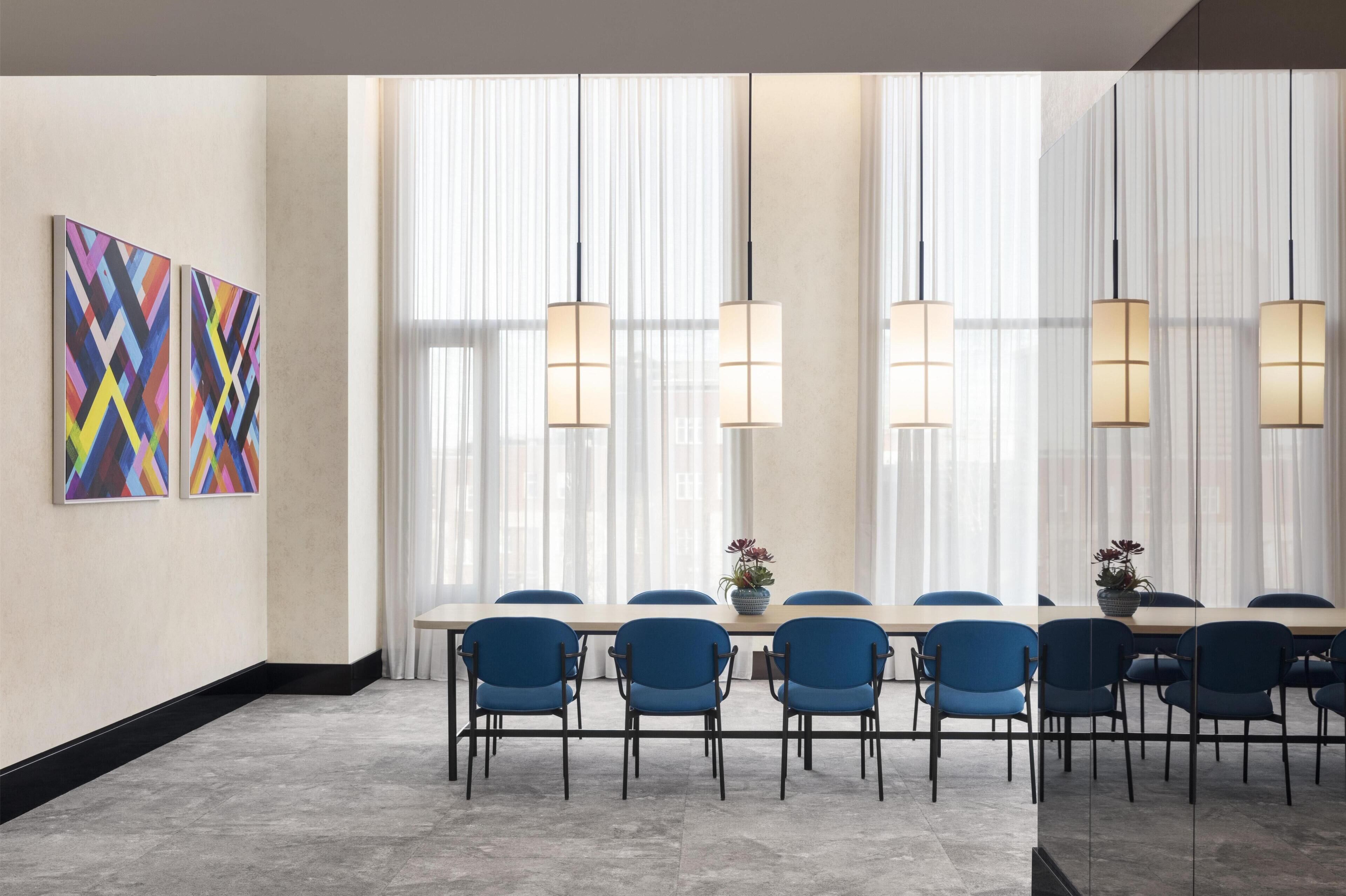 A conference room with a long table, blue chairs, and pendant lights.