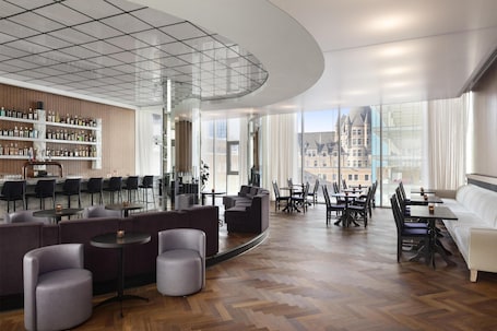 A modern hotel lobby with a bar, seating areas, and large windows offering a city view.
