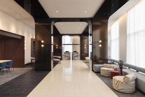 A modern hotel lobby with a central reception desk, seating areas, and a view of the outside.