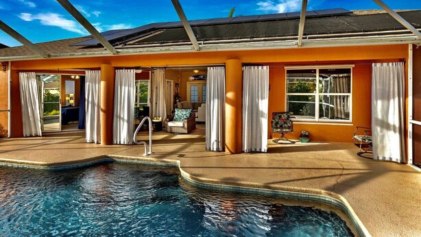 Un área de piscina con techo de vidrio, un salón con sofá y sillones, y vistas al exterior.