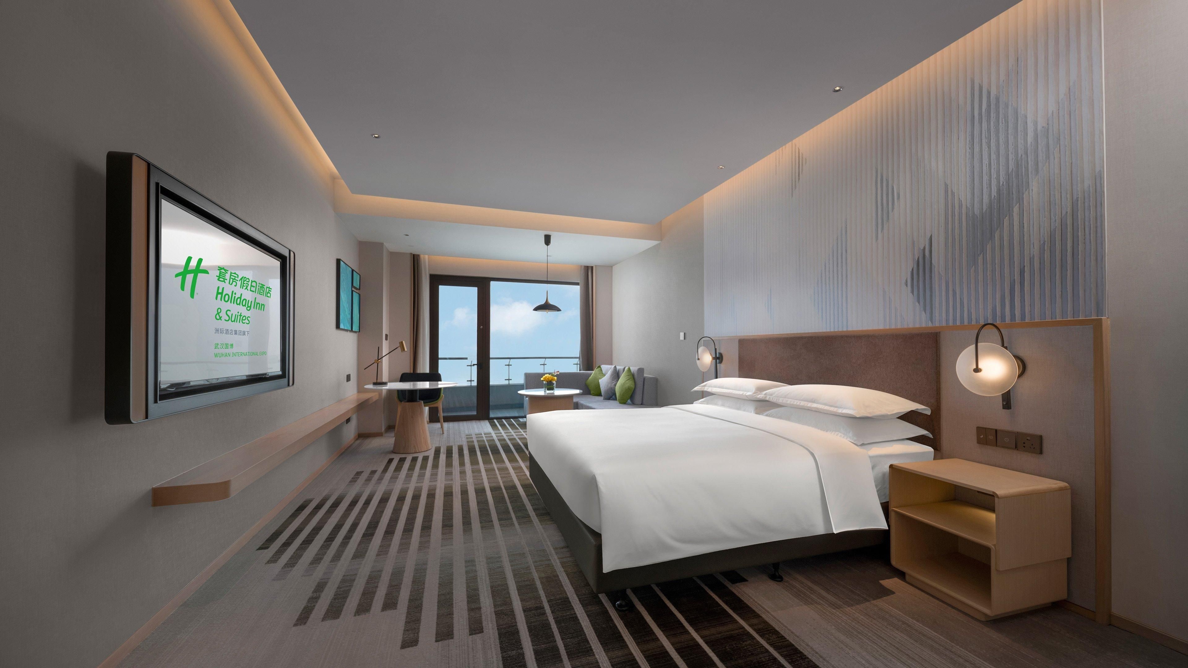 A modern hotel room with a large bed, a desk, and a view of the outdoors.