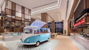 Una furgoneta de estilo retro exhibida en un interior moderno con piso de cuadros, paneles de madera y un ventanal grande.