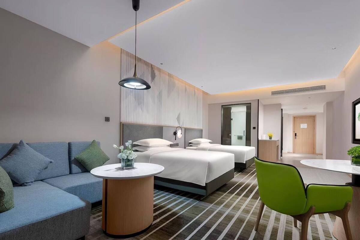 Une chambre d’hôtel moderne avec un canapé, deux lits, une table ronde et une chaise verte.