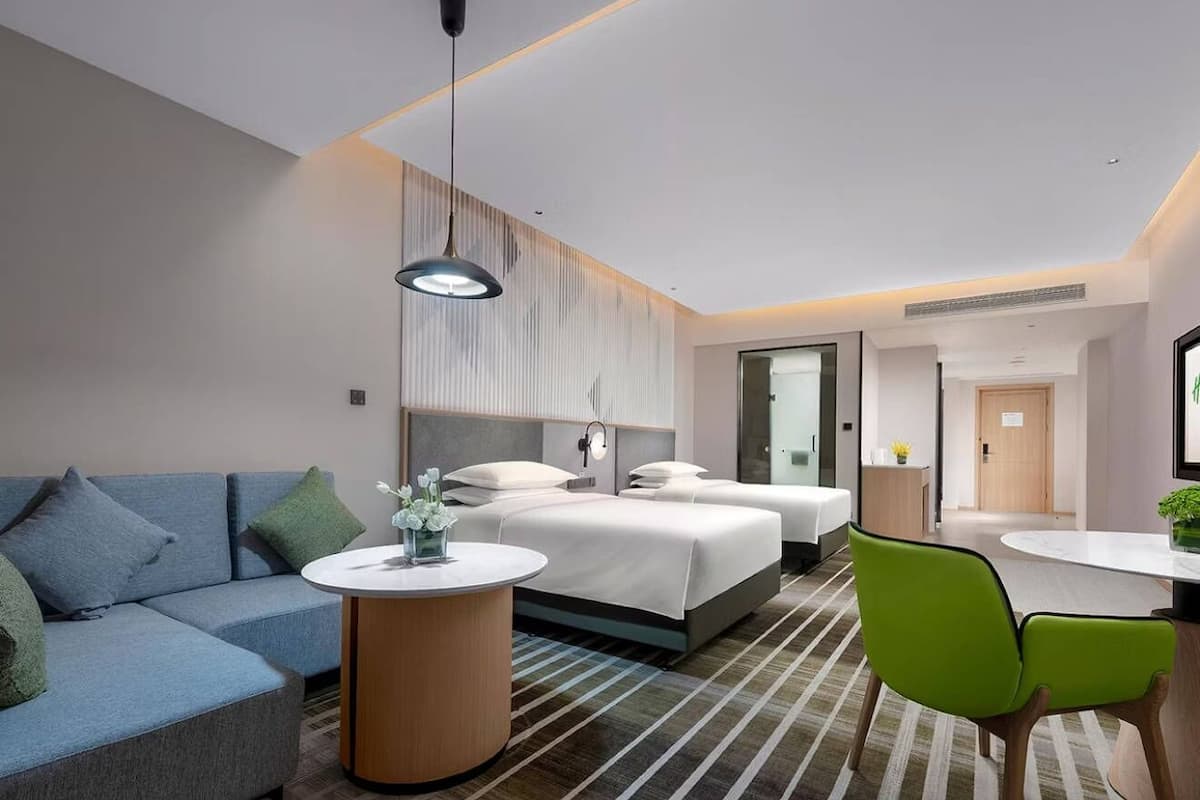 Una habitación de hotel moderna con un sofá, dos camas, una mesa redonda y una silla verde.