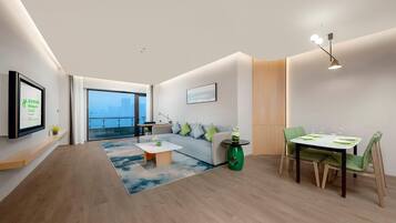Quarto de hotel moderno com sofá, mesa de jantar e uma grande janela com vista para a cidade.