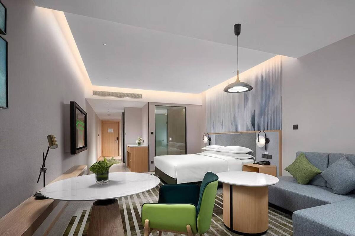 Une chambre d’hôtel moderne comprenant un lit, deux tables de chevet, un canapé, une table de salle à manger ronde et une chaise.