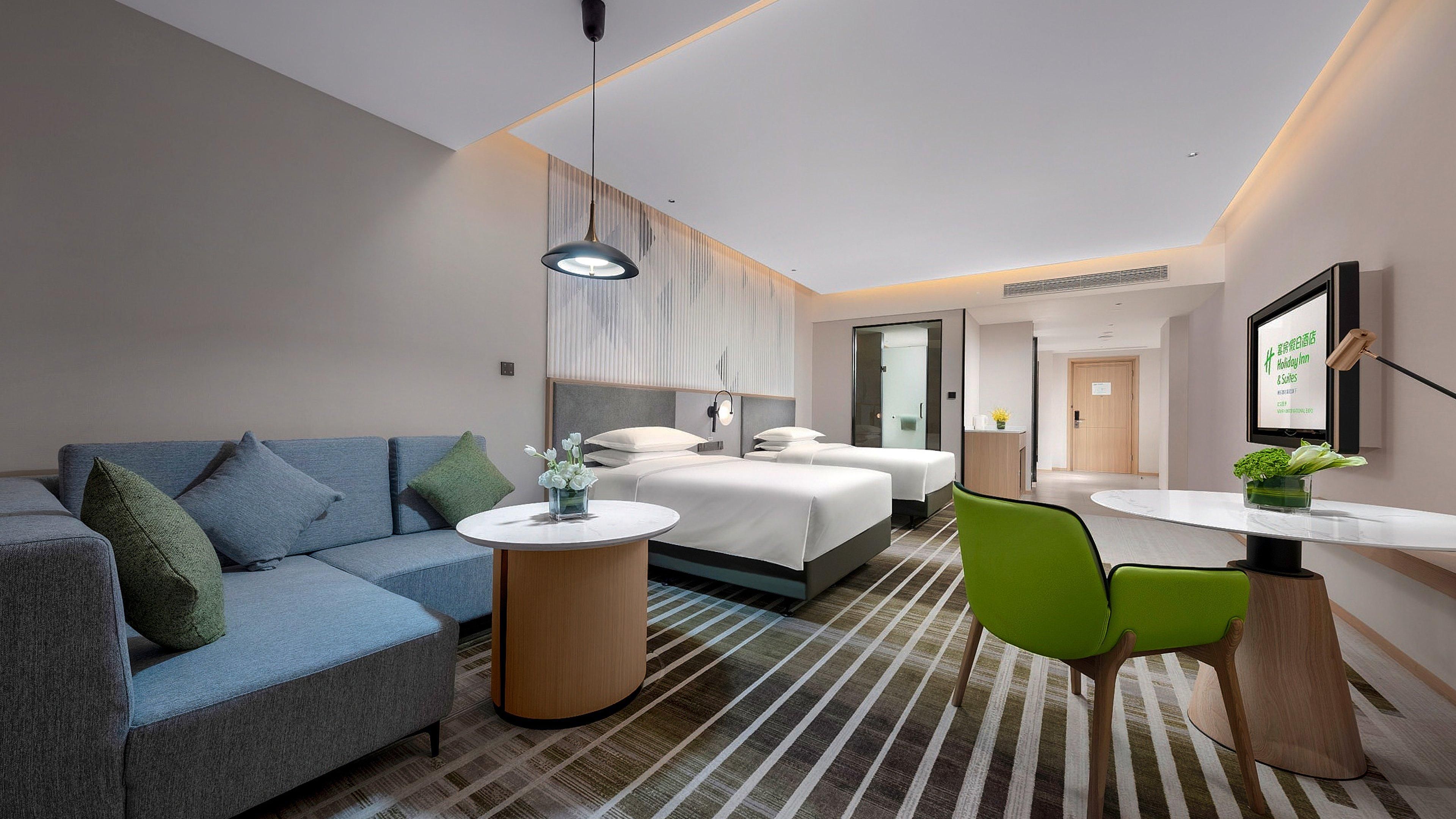 Een moderne hotelkamer met een bank, twee bedden, een eettafel en een televisie.