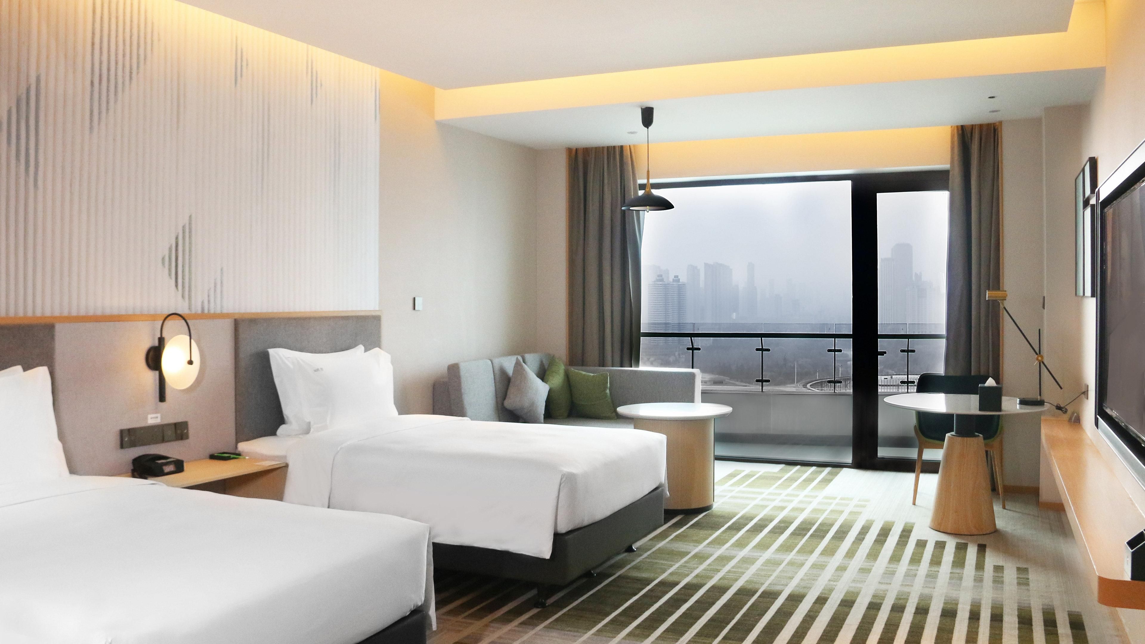 Habitación de hotel con dos camas, un sofá, una mesita y un balcón con vista a la ciudad.