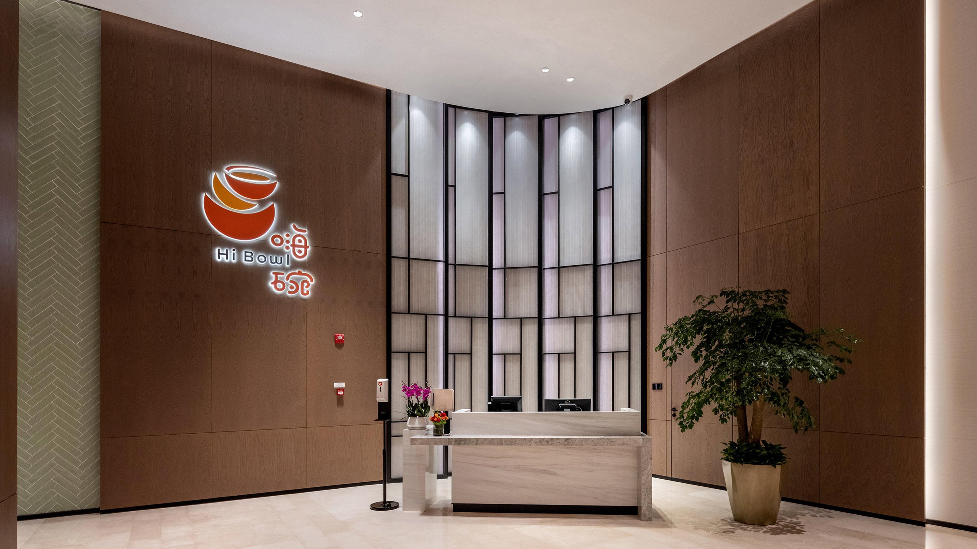 A modern reception area with a wooden wall, a reception desk, a potted plant, and a logo with 'Hi Bowl' and Chinese characters.