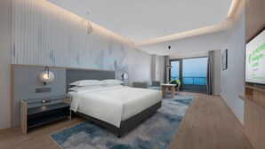 Ein modernes Hotelzimmer mit einem großen Bett, einem Schreibtisch, einem Stuhl und Meerblick.