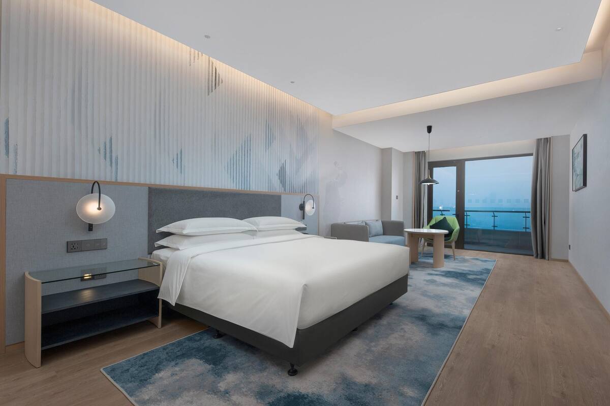 Une chambre d’hôtel moderne, dotée d’un grand lit, d’un bureau, d’une chaise et offrant une vue sur la mer.