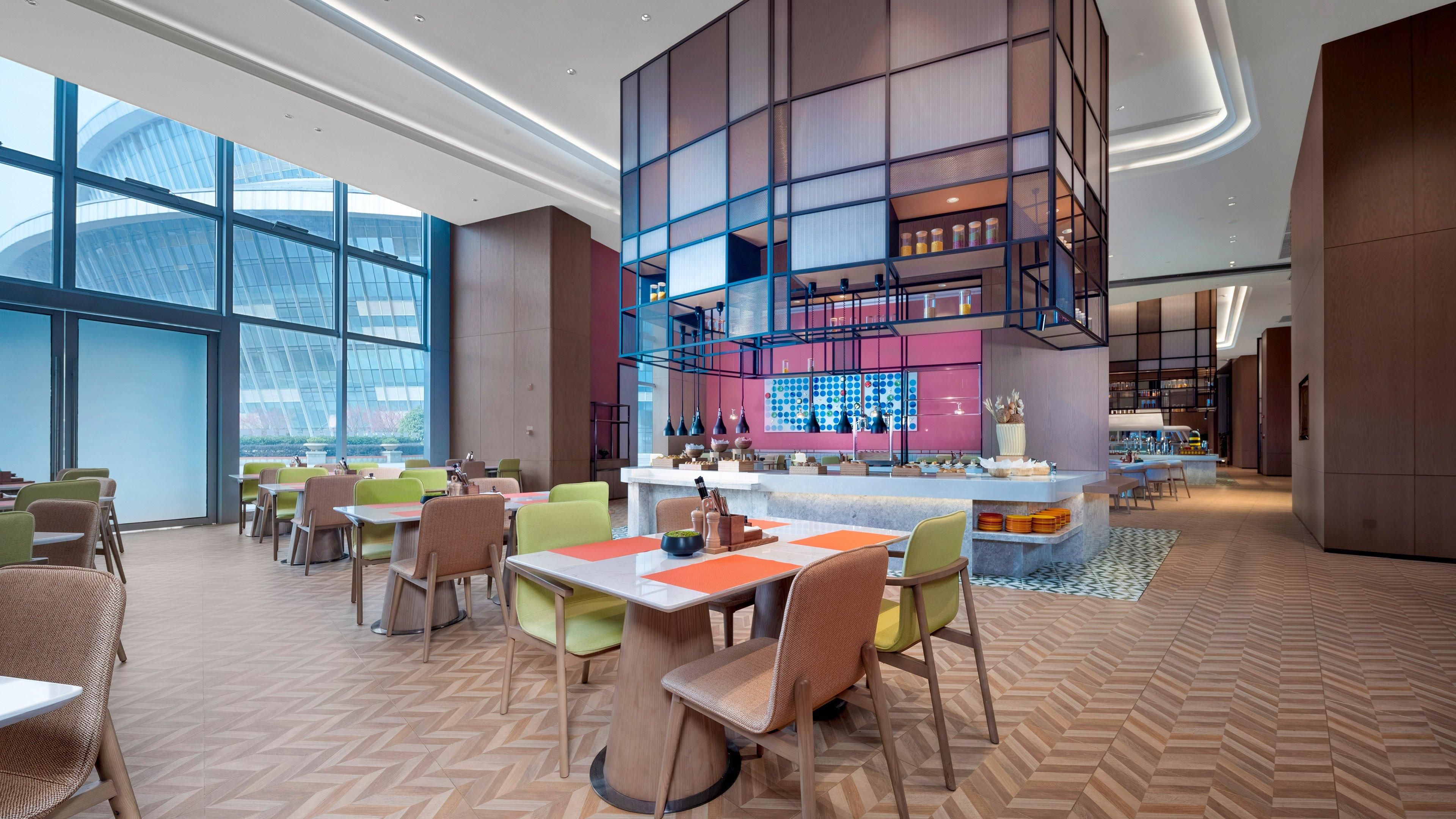 A modern restaurant with a high ceiling, large windows, and a central bar area.