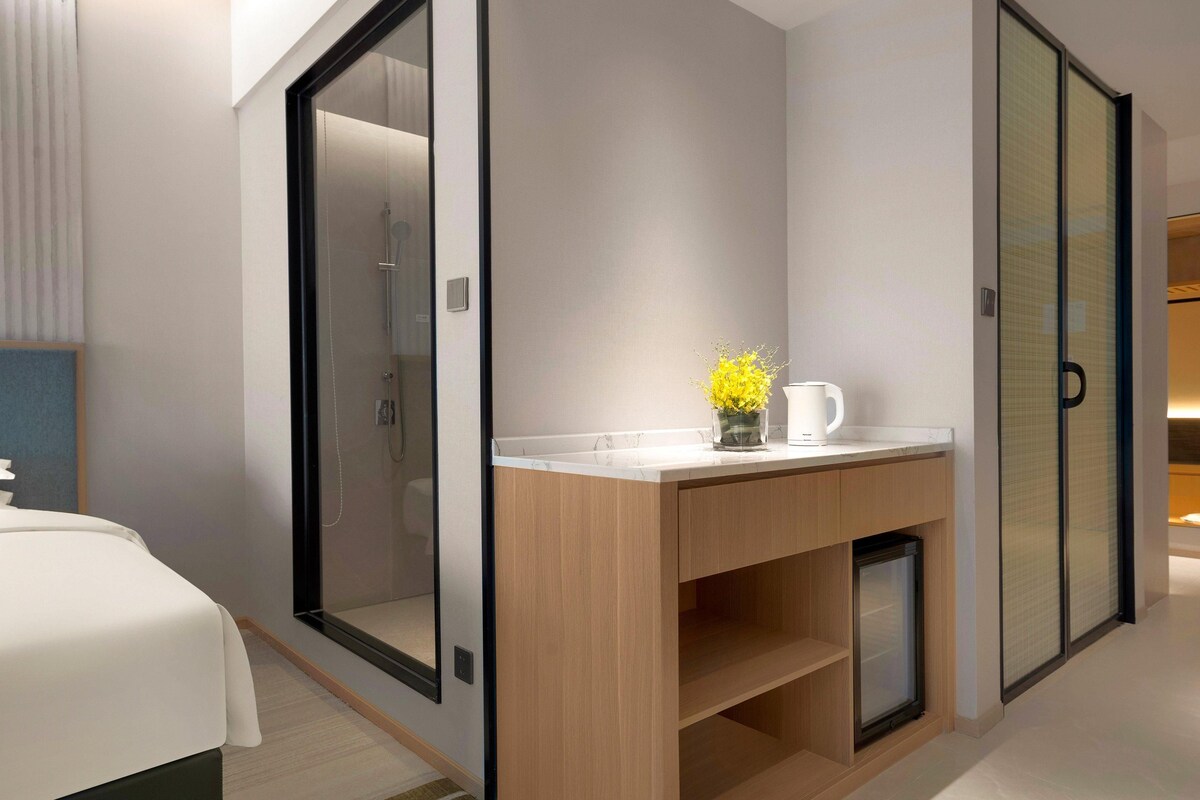 Ein modernes Hotelzimmer mit Bett, einem hölzernen Waschtisch mit Spiegel, einem kleinen Waschbecken und einer Duschkabine.