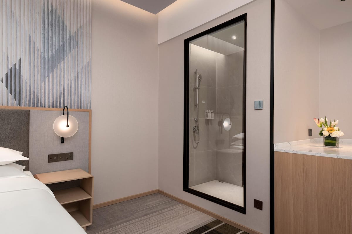 Une chambre d’hôtel moderne équipée d’un lit, d’une douche, d’une coiffeuse avec un miroir et d’un luminaire fixé au mur.