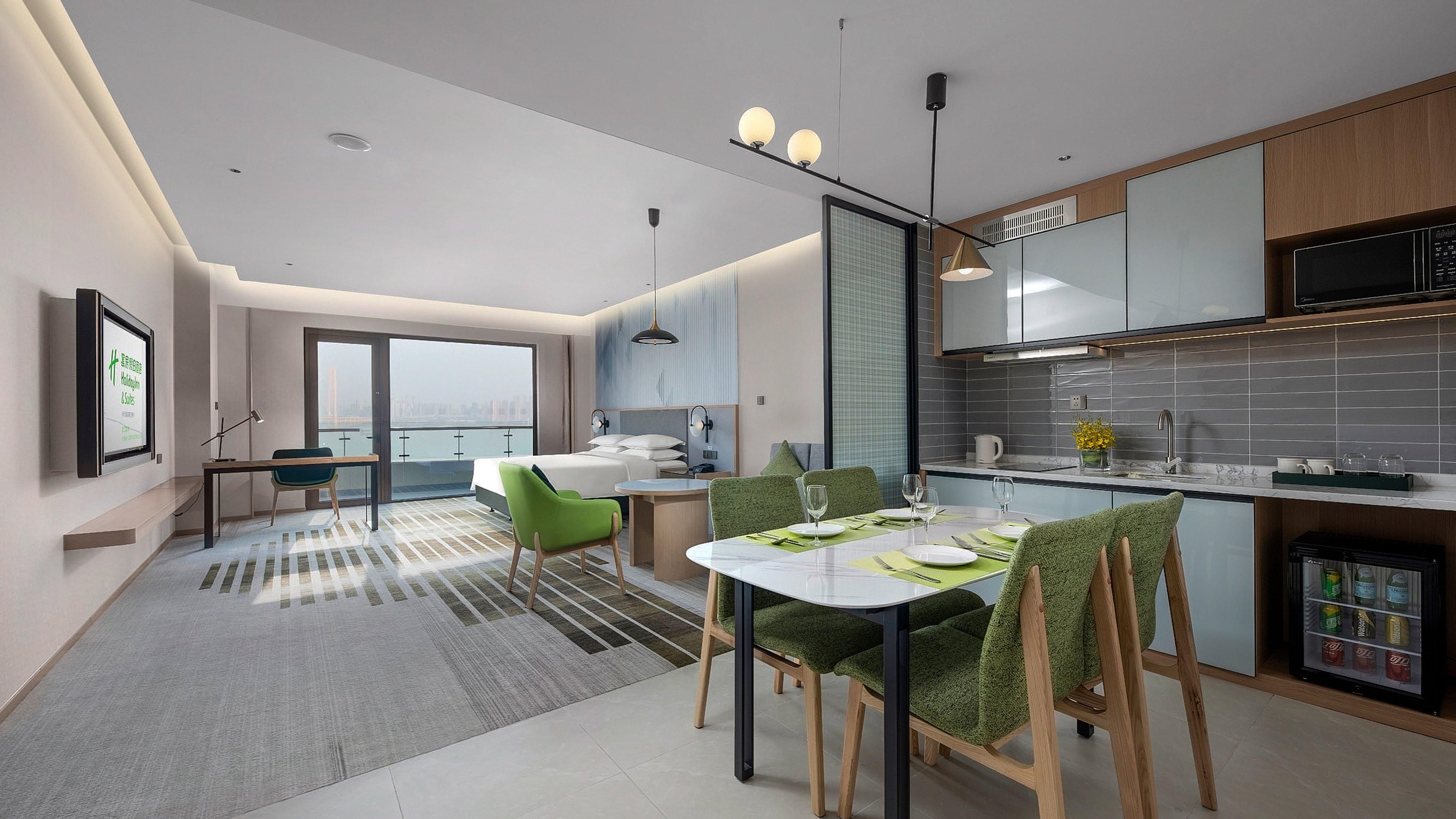 Quarto de hotel moderno com área de refeições, cozinha e vista para a cidade.