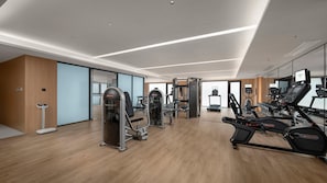 Una palestra moderna con macchinari cardio, attrezzature per l'allenamento con i pesi e una parete a specchio.