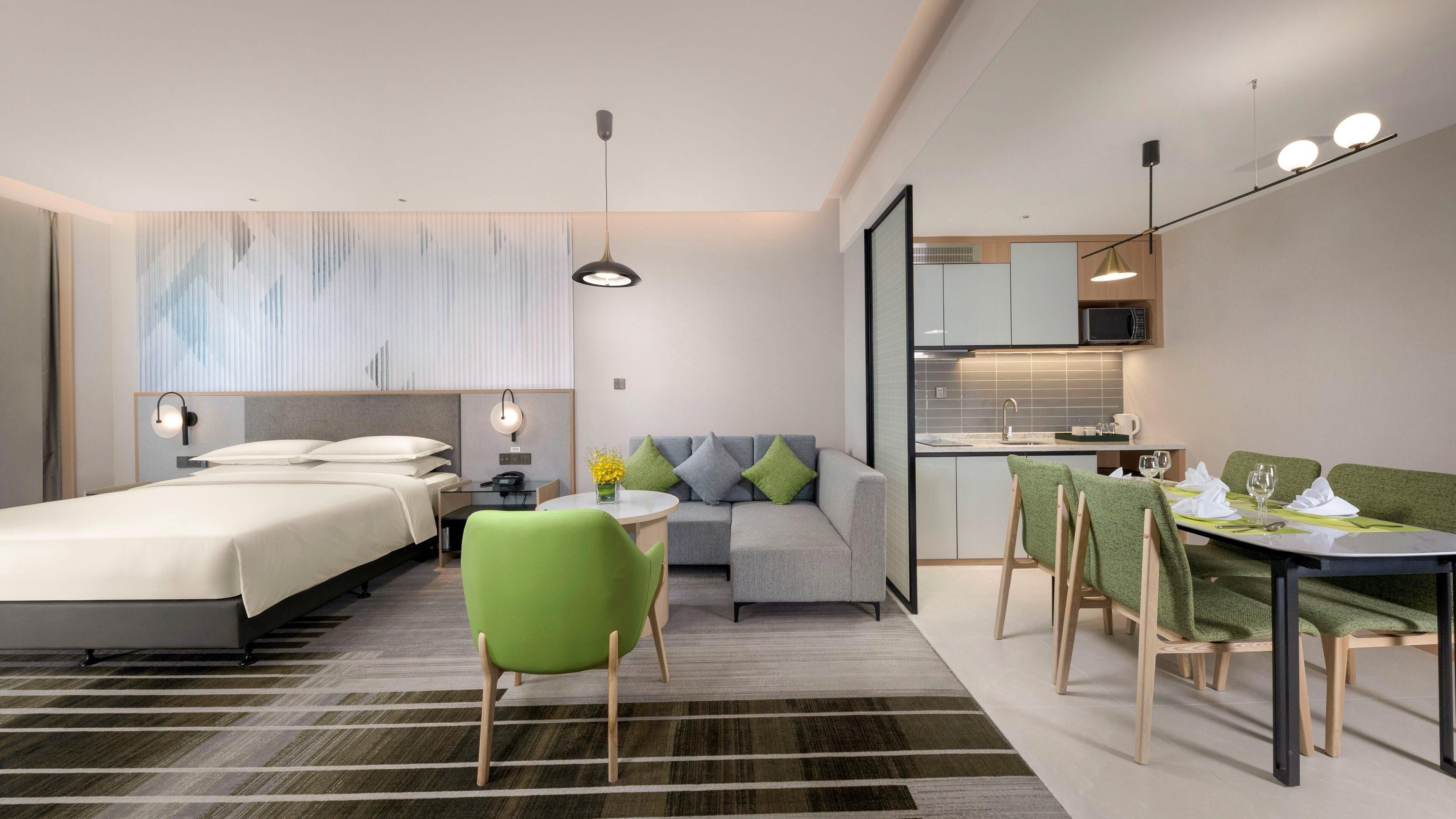 Una habitación de hotel moderna con cama, sofá, mesa de comedor con sillas, una pequeña cocina y baño.