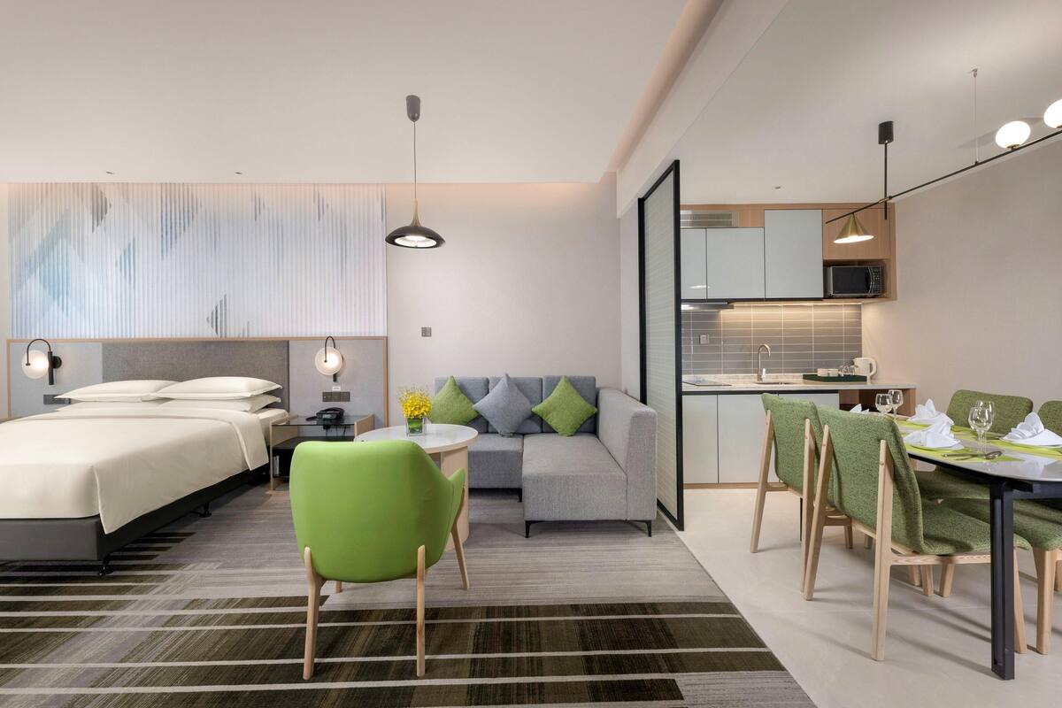 Une chambre d’hôtel moderne comprenant un lit, un canapé, une table à manger avec des chaises, un petit coin cuisine et une salle de bain.