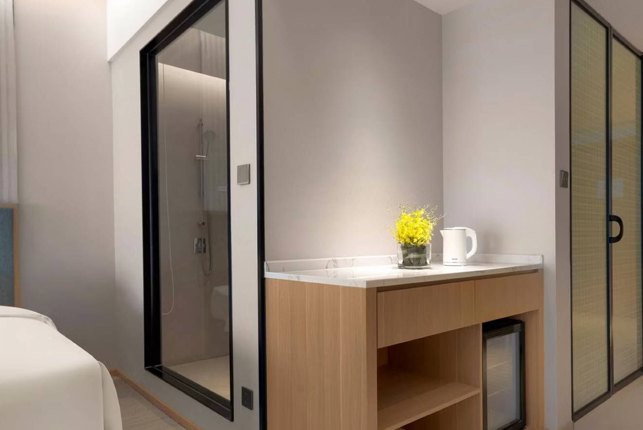 Un baño moderno con cabina de ducha de vidrio, tocador de madera con encimera blanca y un estante pequeño.