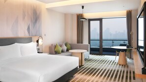 A hotel room with a large bed, a sofa, a small table, and a balcony with a view of the city. - Holiday Inn Hotel & Sts Wuhan International Expo (Wuhan)