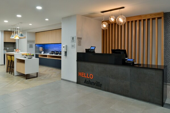 Un mostrador de recepción moderno con un cartel que dice "HELLO Asheville", una pantalla digital y un revestimiento de pared de madera.