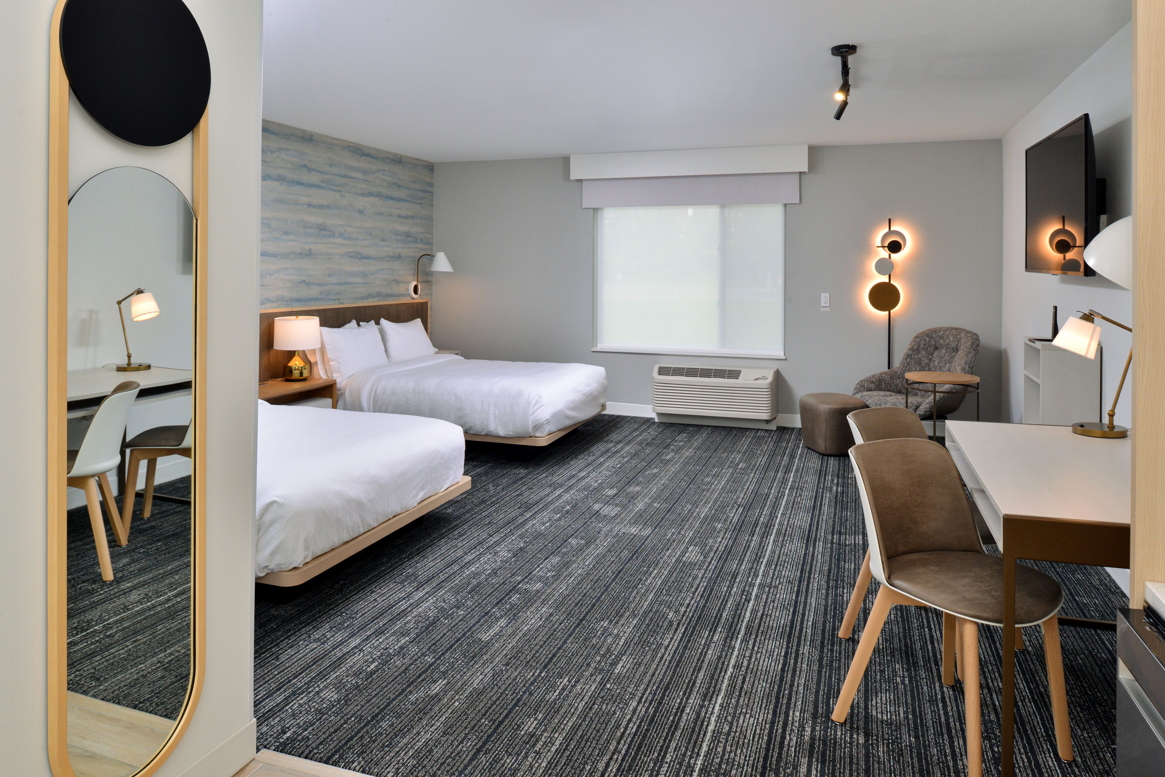 Hotellihuone, jossa on kaksi sänkyä, työpöytä, tuoli, televisio ja suuri peili.