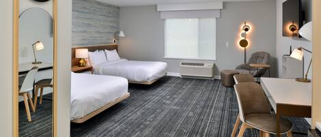 Hotellihuone, jossa on kaksi sänkyä, työpöytä, tuoli, televisio ja suuri peili.