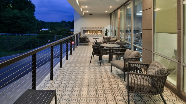 A balcony with a patterned floor, wicker furniture, and a view of the road and trees. - TownePlace Suites by Marriott Asheville Downtown (Asheville)