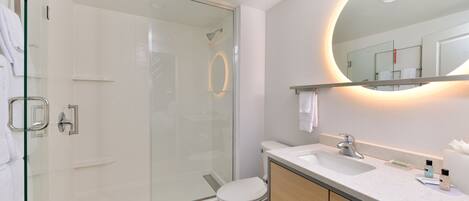 A modern bathroom with a glass shower enclosure, a toilet, a sink, and a mirror with a circular light.