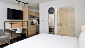A hotel room with a bed, a desk, a chair, a TV, a microwave, and a shower area. - TownePlace Suites by Marriott Asheville Downtown (Asheville)