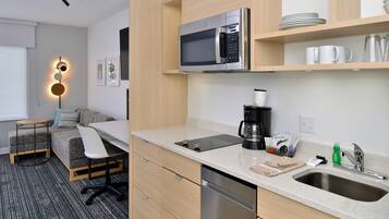 A compact kitchen with a microwave, coffee maker, and sink. There is a small dining area with a chair and a table.