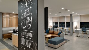 A modern hotel lobby with a black sign reading "A Great Day Starts with Breakfast." There are seating areas with sofas and tables, and a large window providing natural light. - TownePlace Suites by Marriott Asheville Downtown (Asheville)