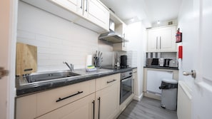 A compact kitchen with white cabinets, a stainless steel sink, a microwave, and a toaster. - Modern Townhouse Apartment in Stratford Upon Avon With Wifi & Netflix (Stratford-upon-Avon)