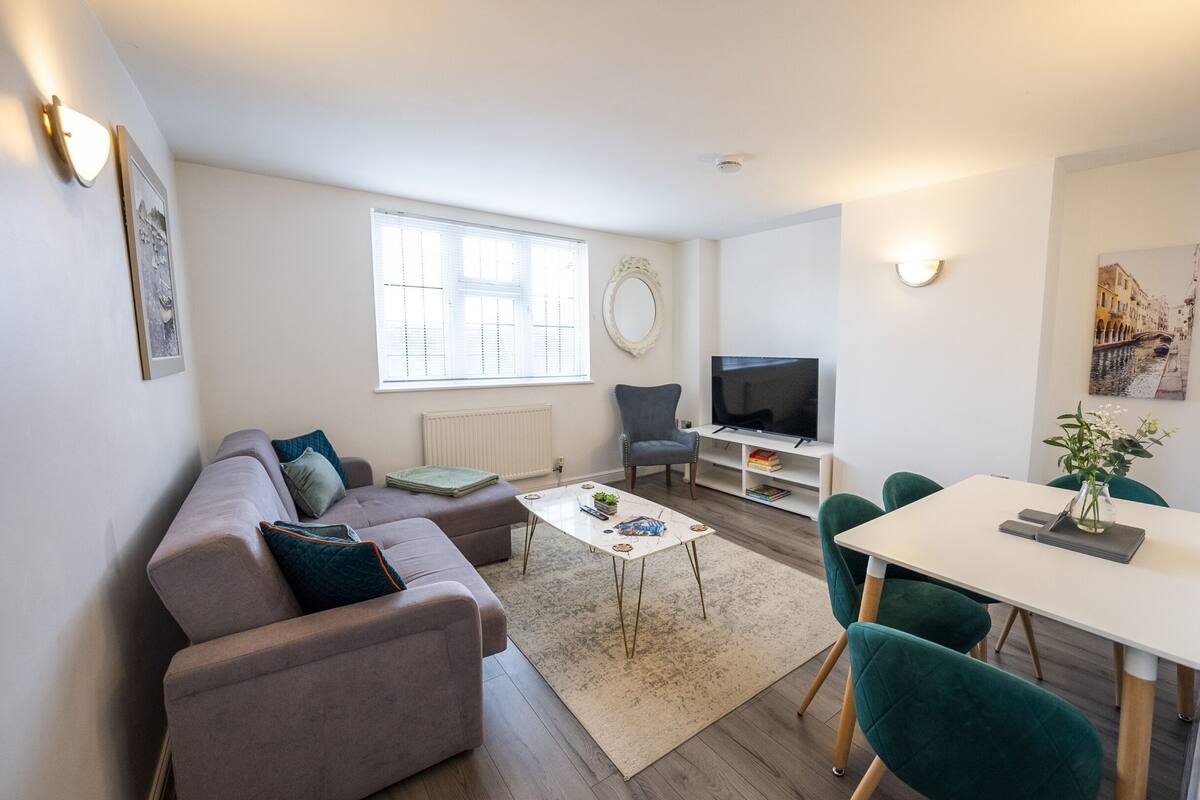 Ein modernes Wohnzimmer mit einer Couch, einem Couchtisch, einem Fernseher und einem Essbereich mit Stühlen und einem Tisch.