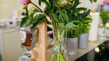 Eine Küchenarbeitsplatte mit einer Vase voller pinkfarbener Blumen, einer Kaffeemaschine und gestapelten weißen Tellern mit grünen Mustern.