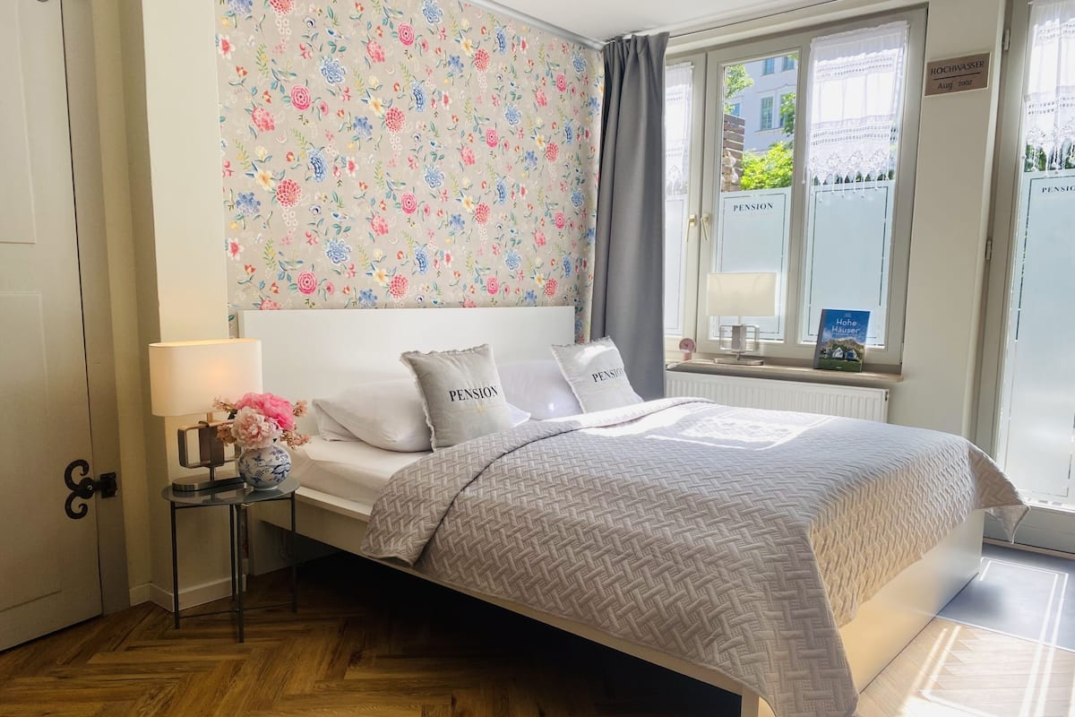 Un dormitorio ordenado con cama, mesita de noche con lámpara y ventana con cortinas.