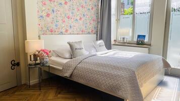Un dormitorio ordenado con cama, mesita de noche con lámpara y ventana con cortinas.