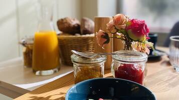 Un desayuno con un tazón de yogur cubierto de bayas, un vaso de jugo de naranja y frascos de mermelada.