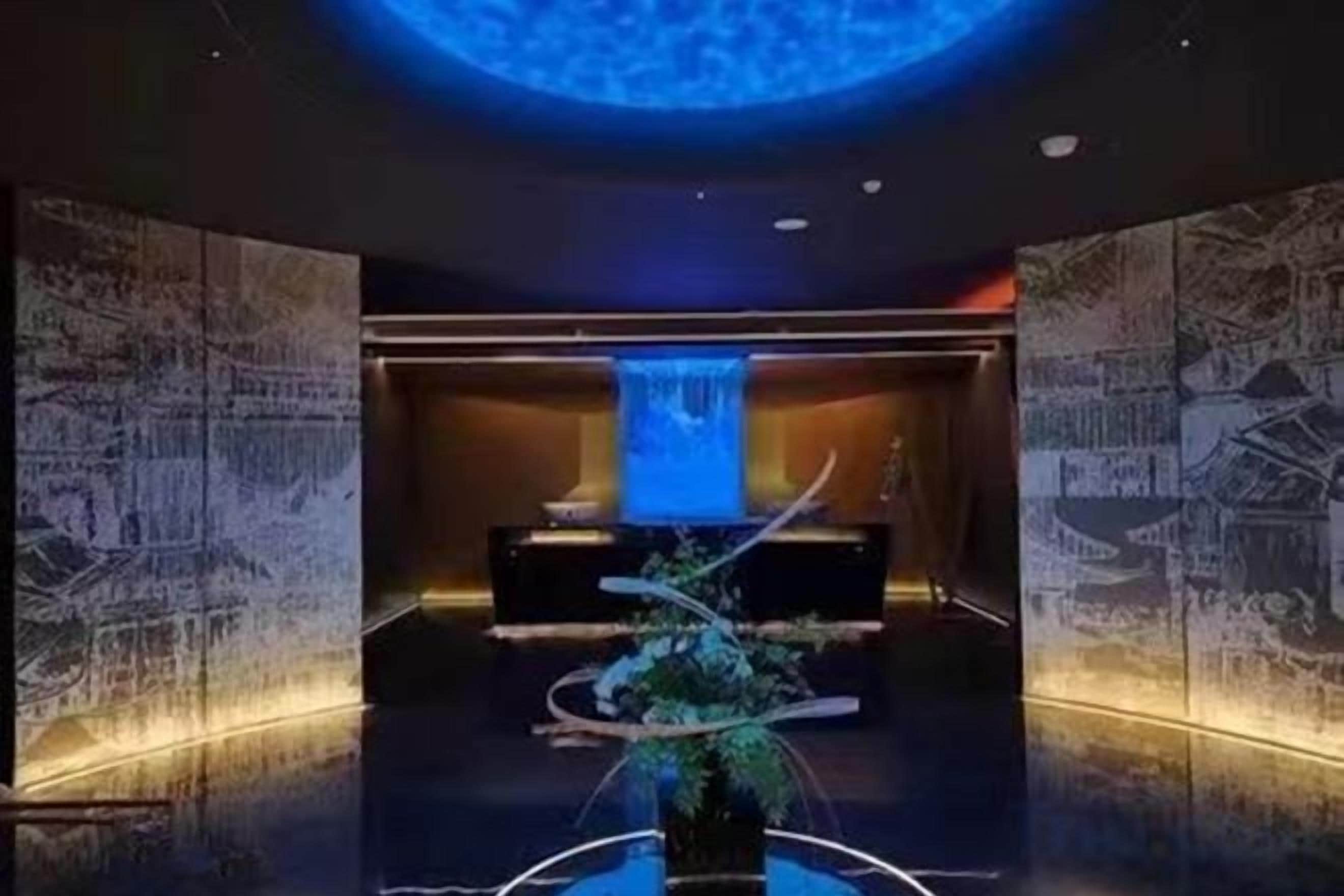 A lobby with a reception desk, a water feature, and a large illuminated wall.