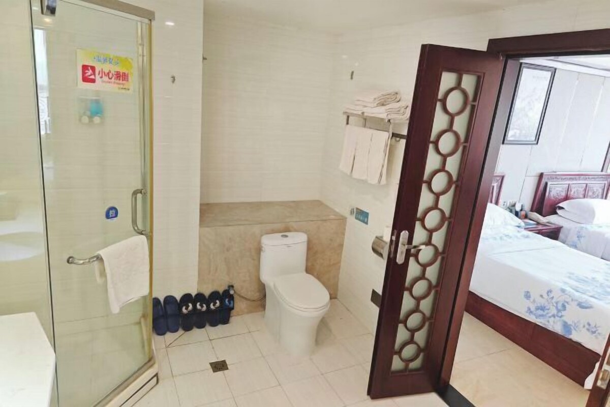 Un baño de hotel con cabina de ducha de vidrio, inodoro y cama con colcha estampada.