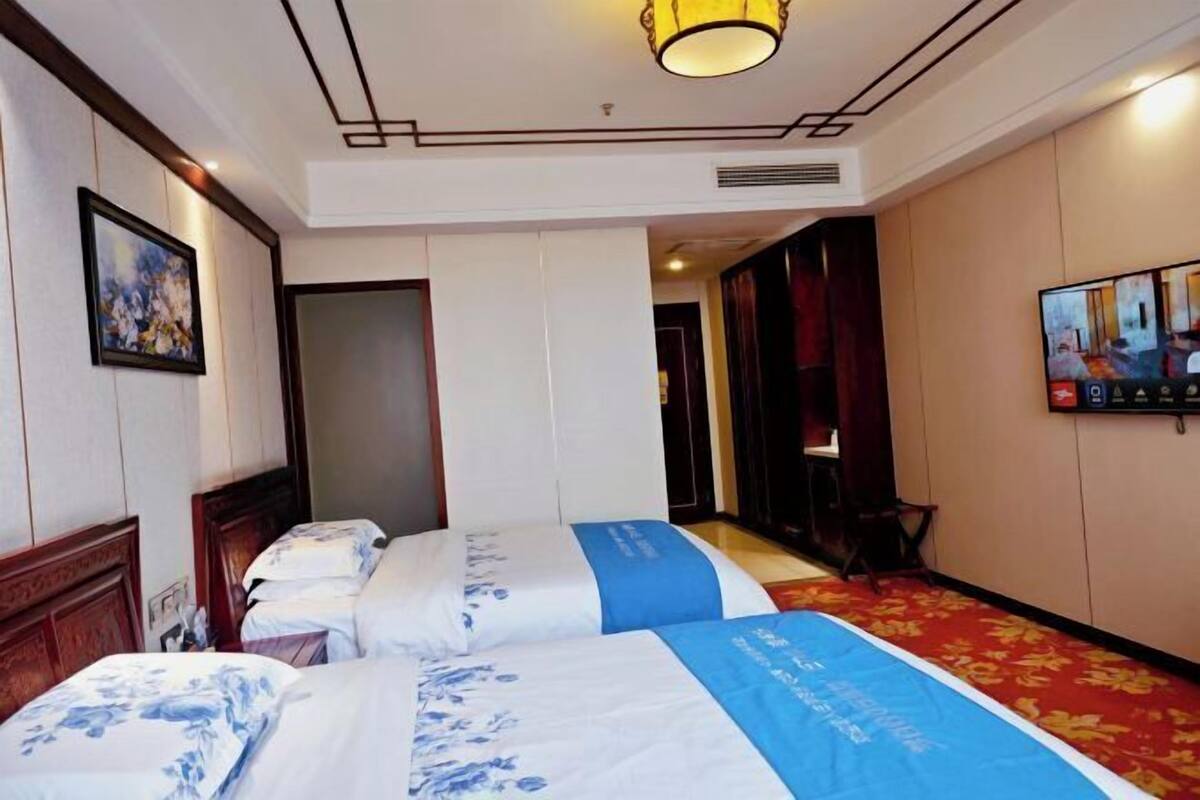 A hotel room with two beds, a television, and a painting on the wall.