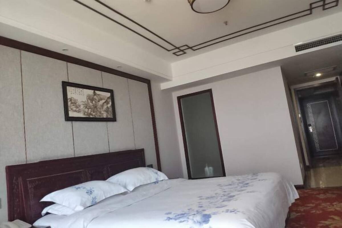 A hotel room with a wooden headboard, a bed with a floral bedspread, a framed picture on the wall, and a red carpeted floor.